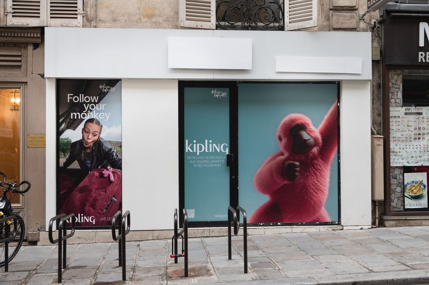 A Paris storefront with vinyl covering the windows, carrying a fashion campaign with a large pink monkey, pointing at a pop-up in a department store.